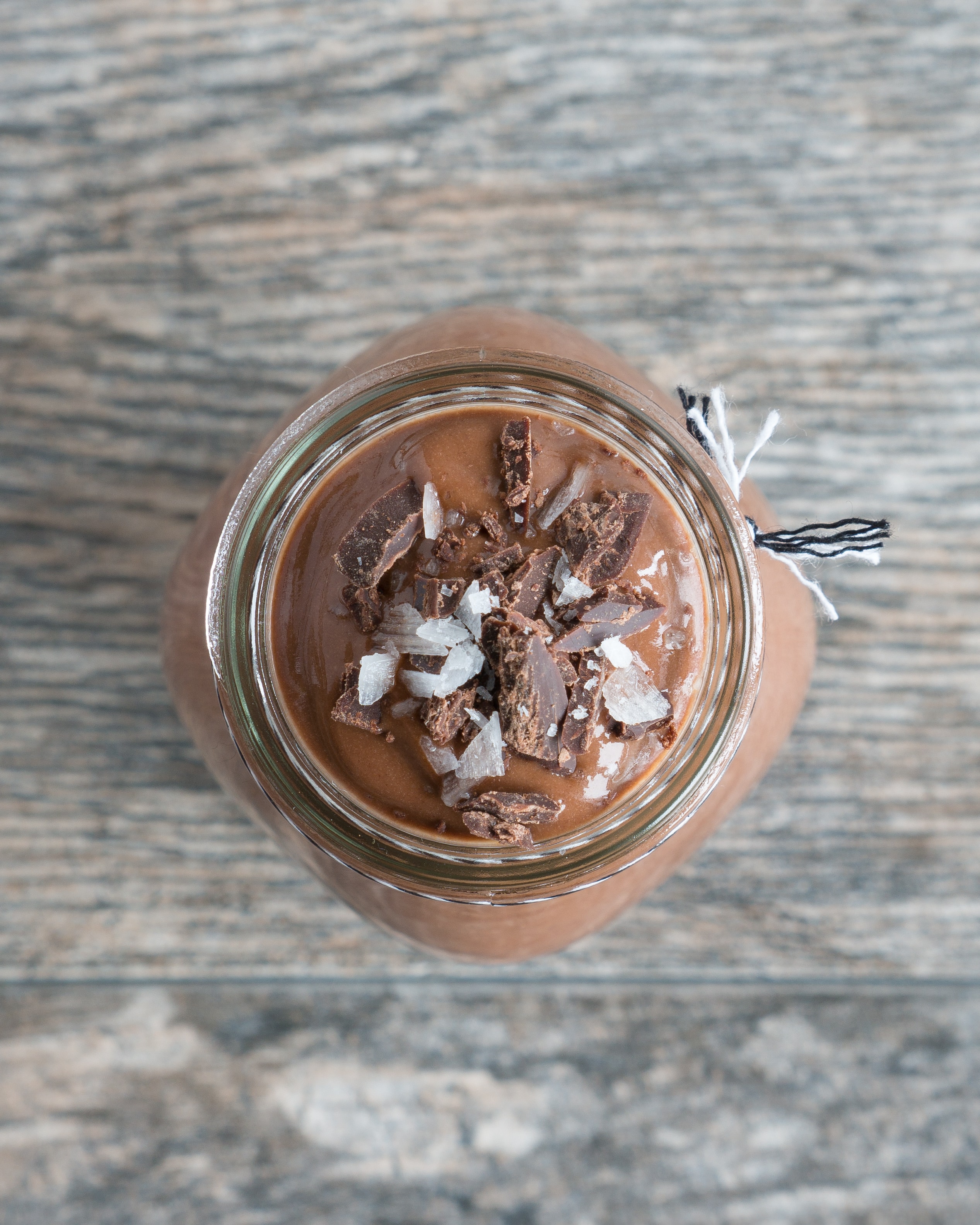Glass of chocolate banana smoothie with chocolate shavings and salt on top with a wood background