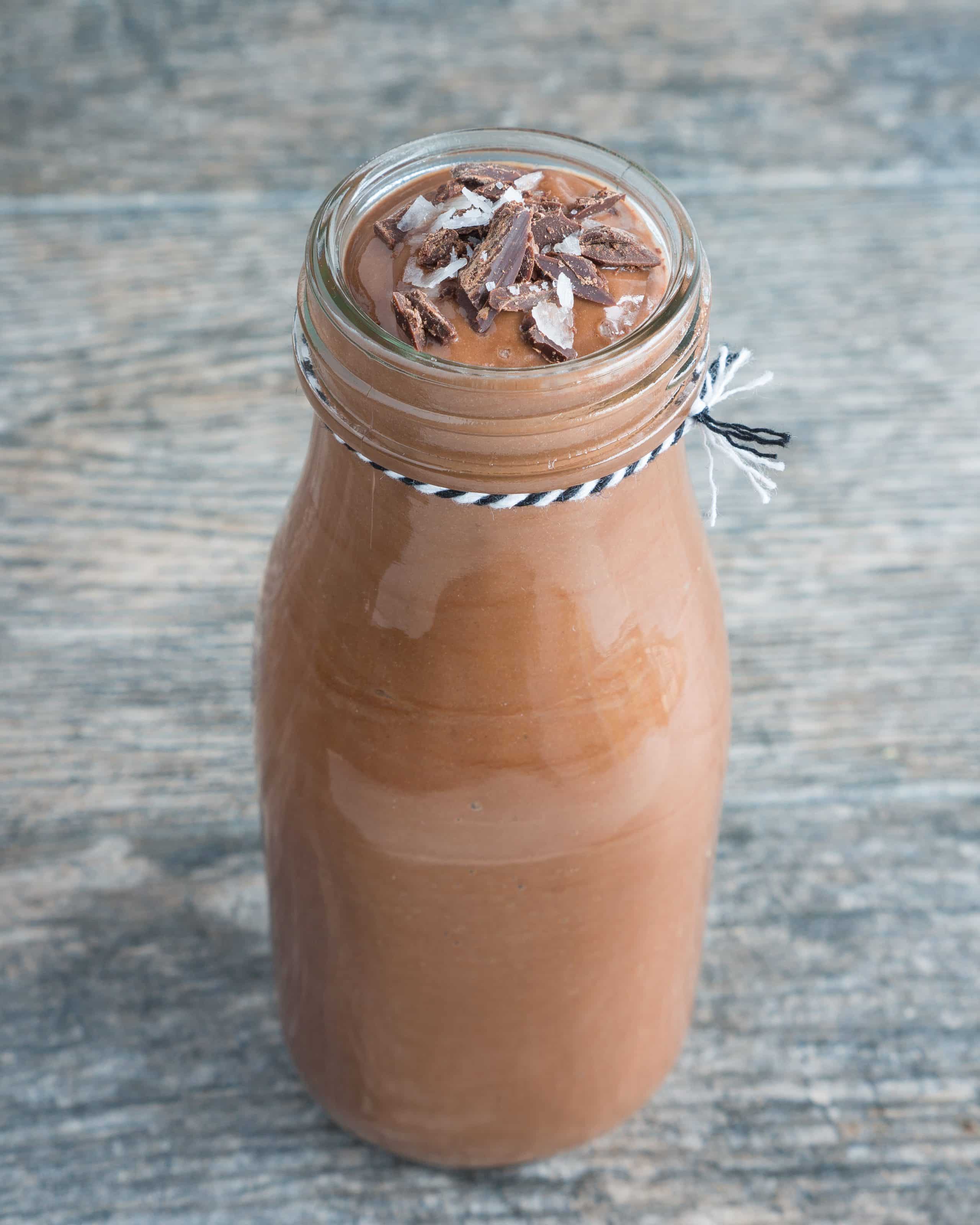 Glass of chocolate banana smoothie with chocolate shavings and salt on top with a wood background