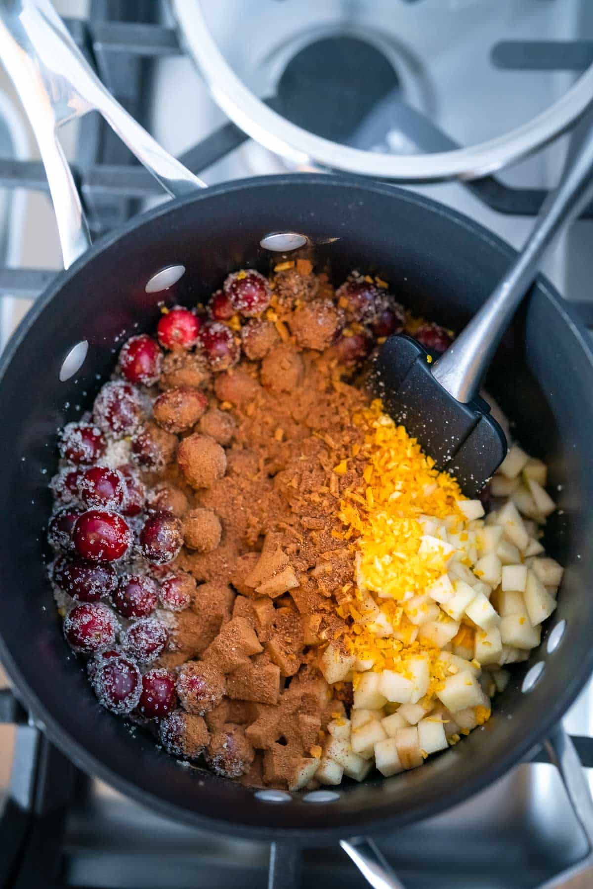 Cranberries, diced apples, and cinnamon layered inside of a black pot on the stove.