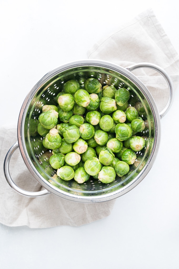 top down view of a metal colander filled with just rinsed Brussels sprouts on a white background