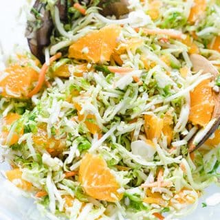 Shaved Brussels Sprout Salad with Oranges in a clear bowl with a wooden spoon