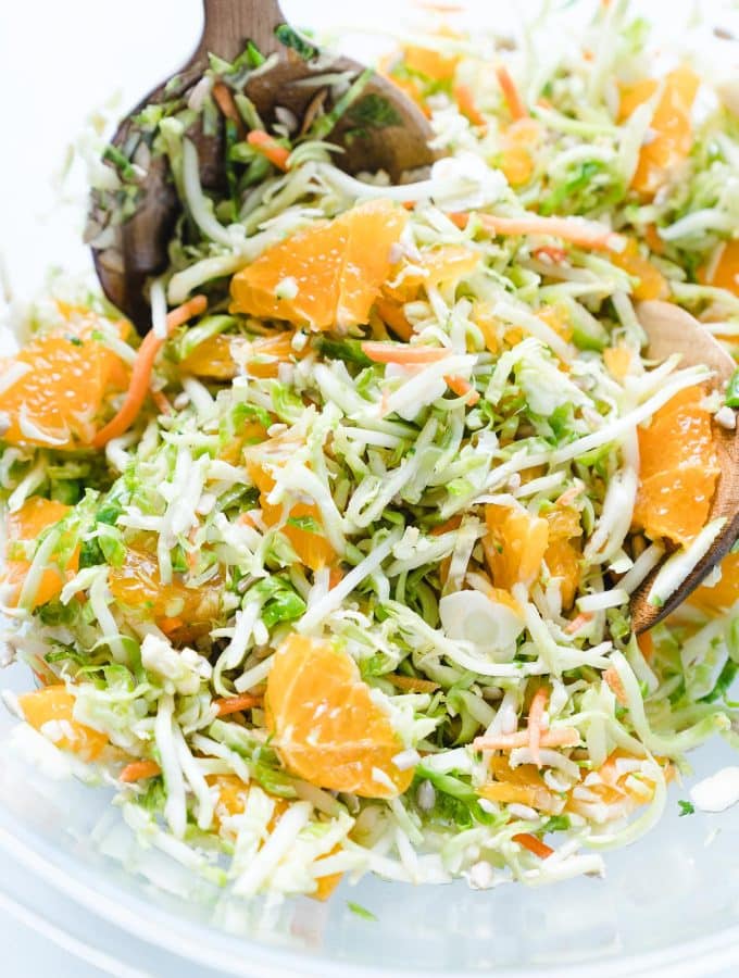 Shaved Brussels Sprout Salad with Oranges in a clear bowl with a wooden spoon