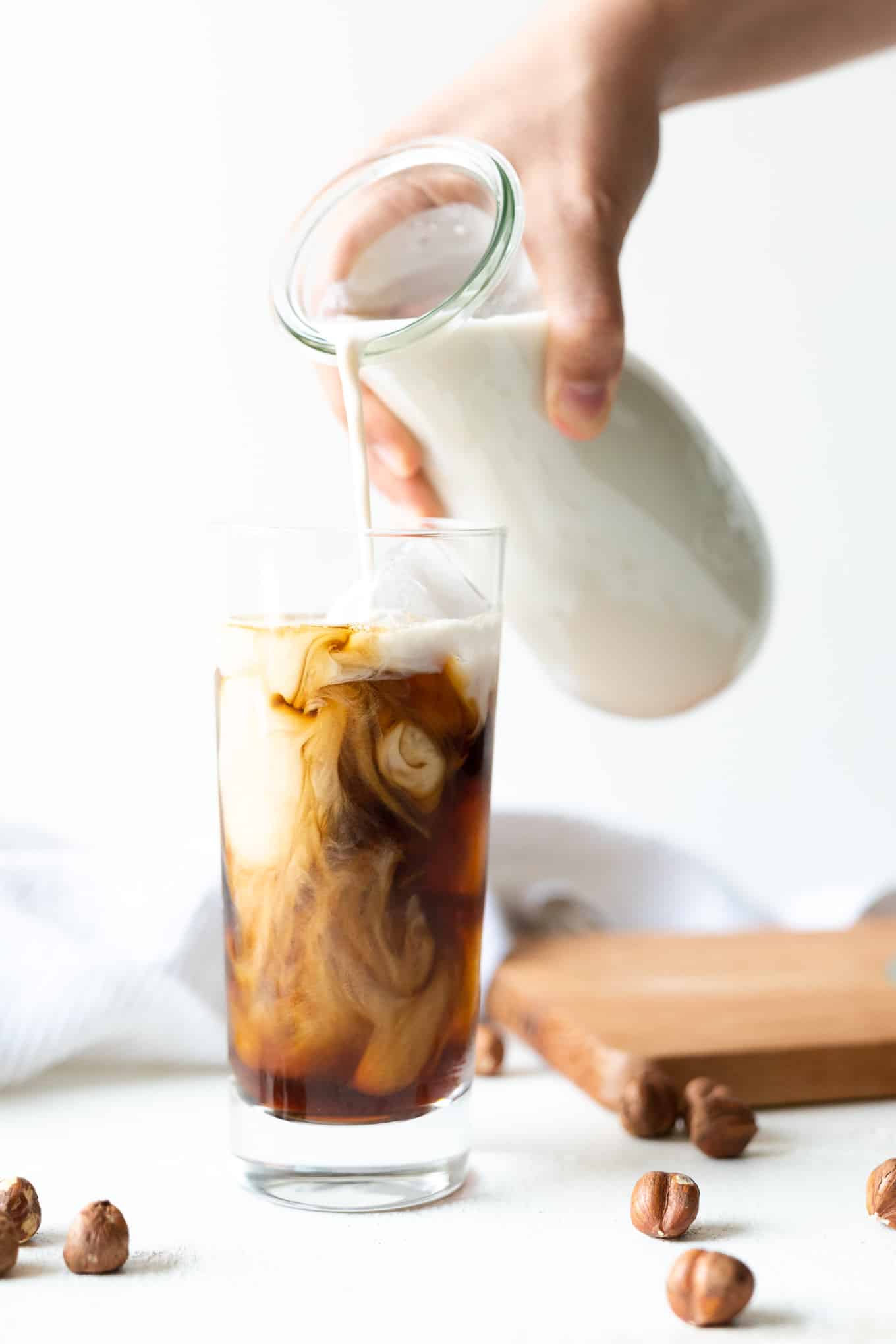 Pouring hazelnut milk into iced coffee in tall glass