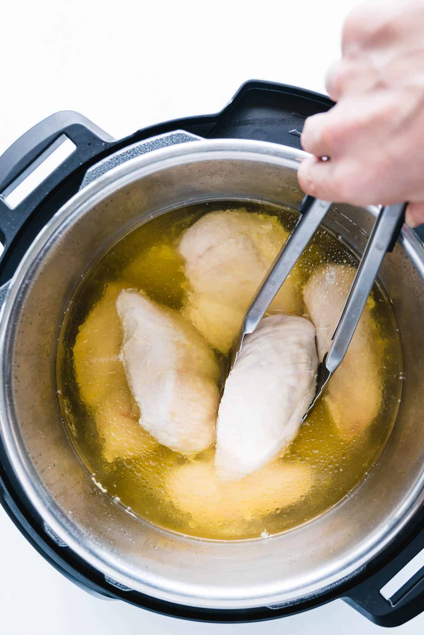 Taking out chicken breasts from instant pot with tongs