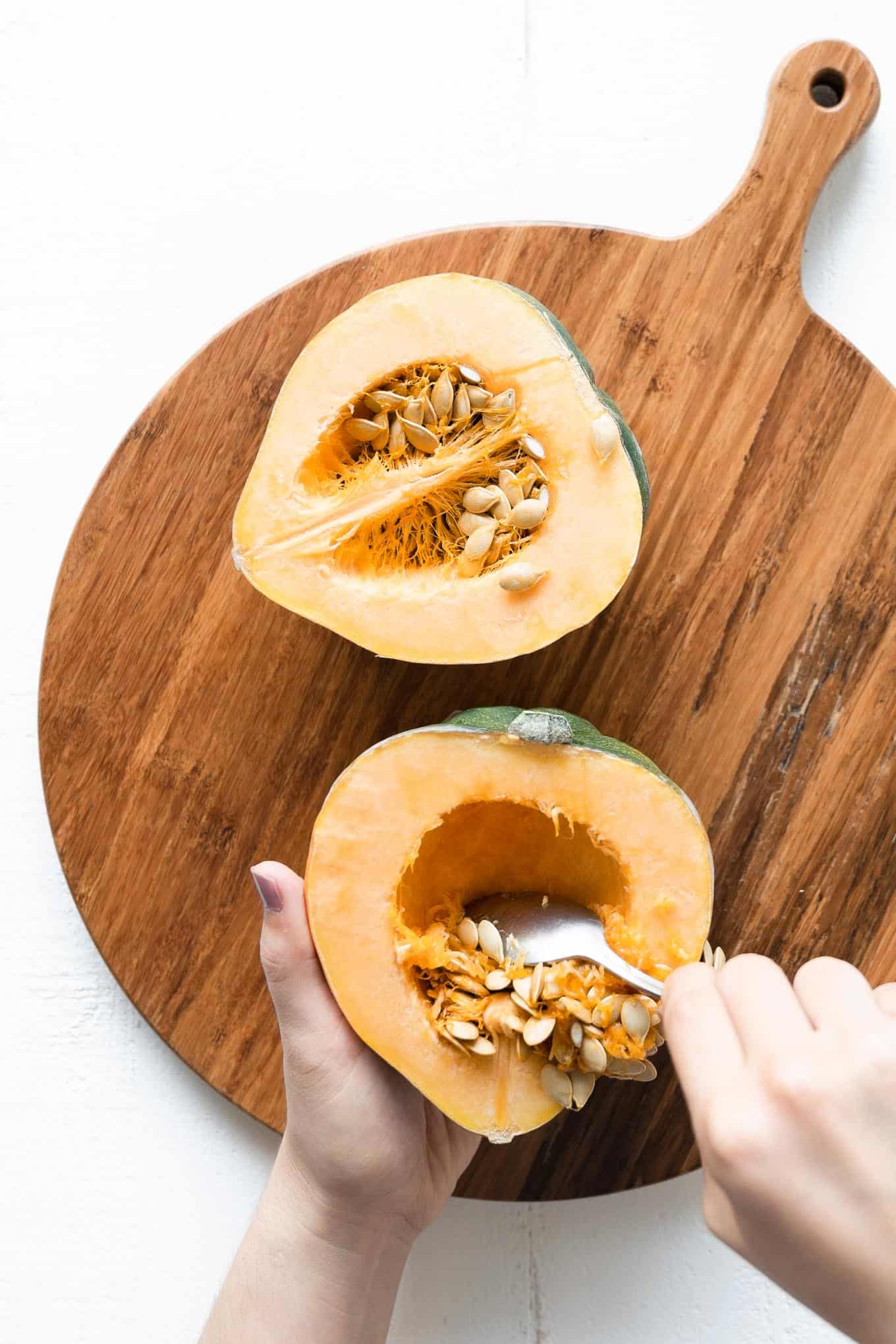 Scraping seeds out of acorn squash half with a spoon
