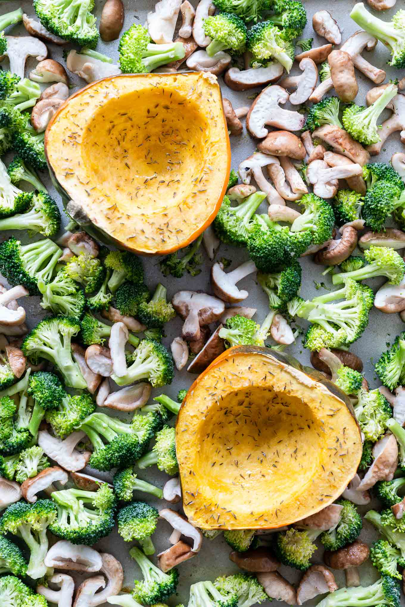 Acorn Squash halves on a sheet tray surrounded by broccoli and mushrooms