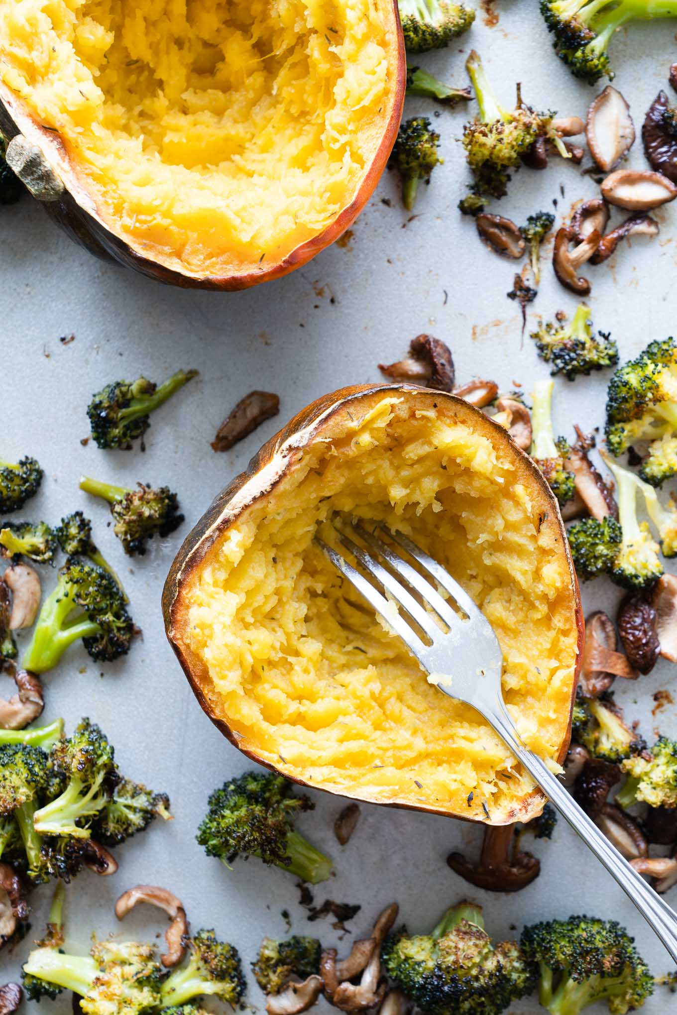 lightly mashed acorn squash on a sheet tray with broccoli and mushrooms
