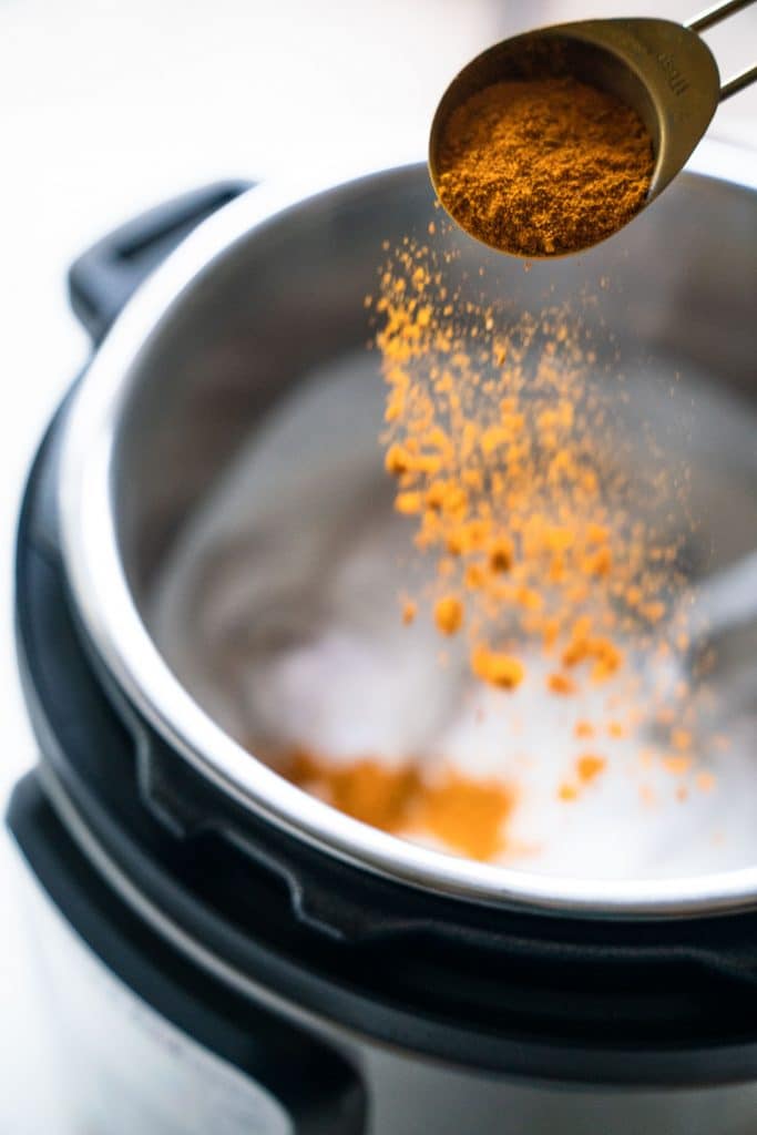 shaking curry powder over top coconut milk and chicken in instant pot