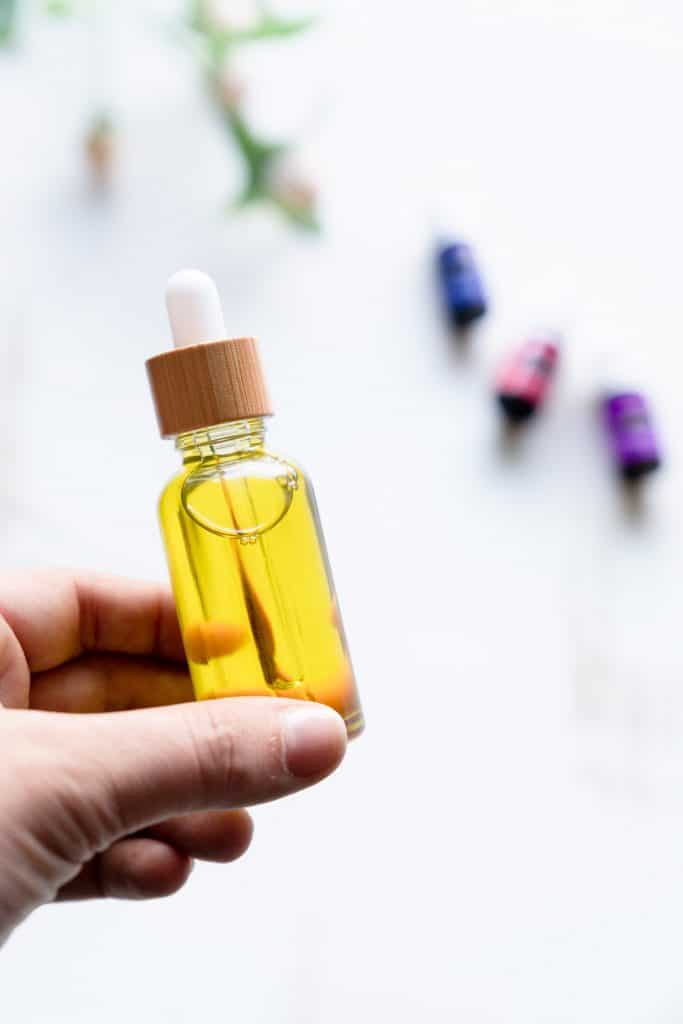 holding yellow face serum in glass bottle