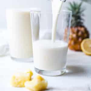 Creamy pineapple banana smoothie being poured into two glasses.