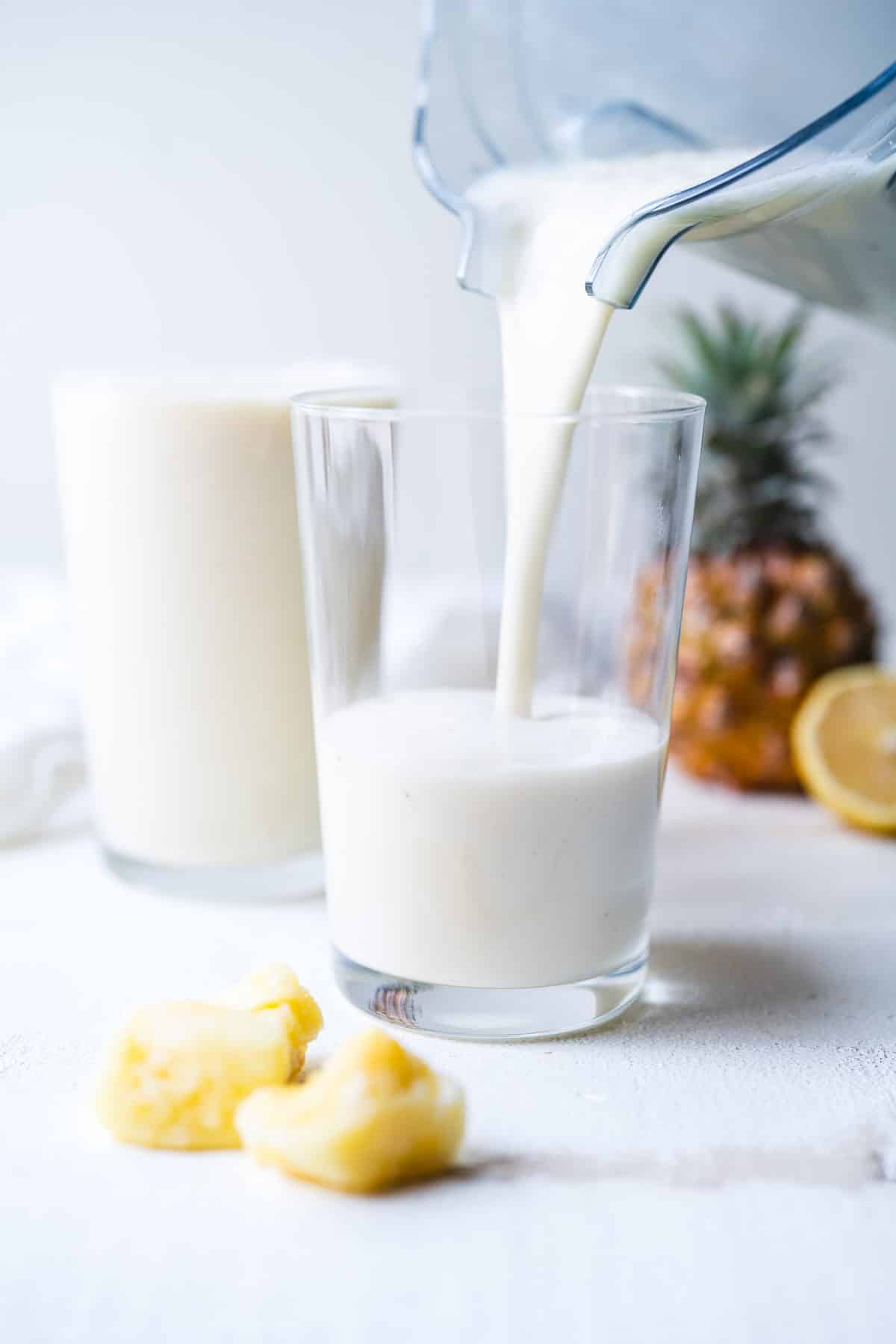 Creamy pineapple banana smoothie being poured into two glasses.