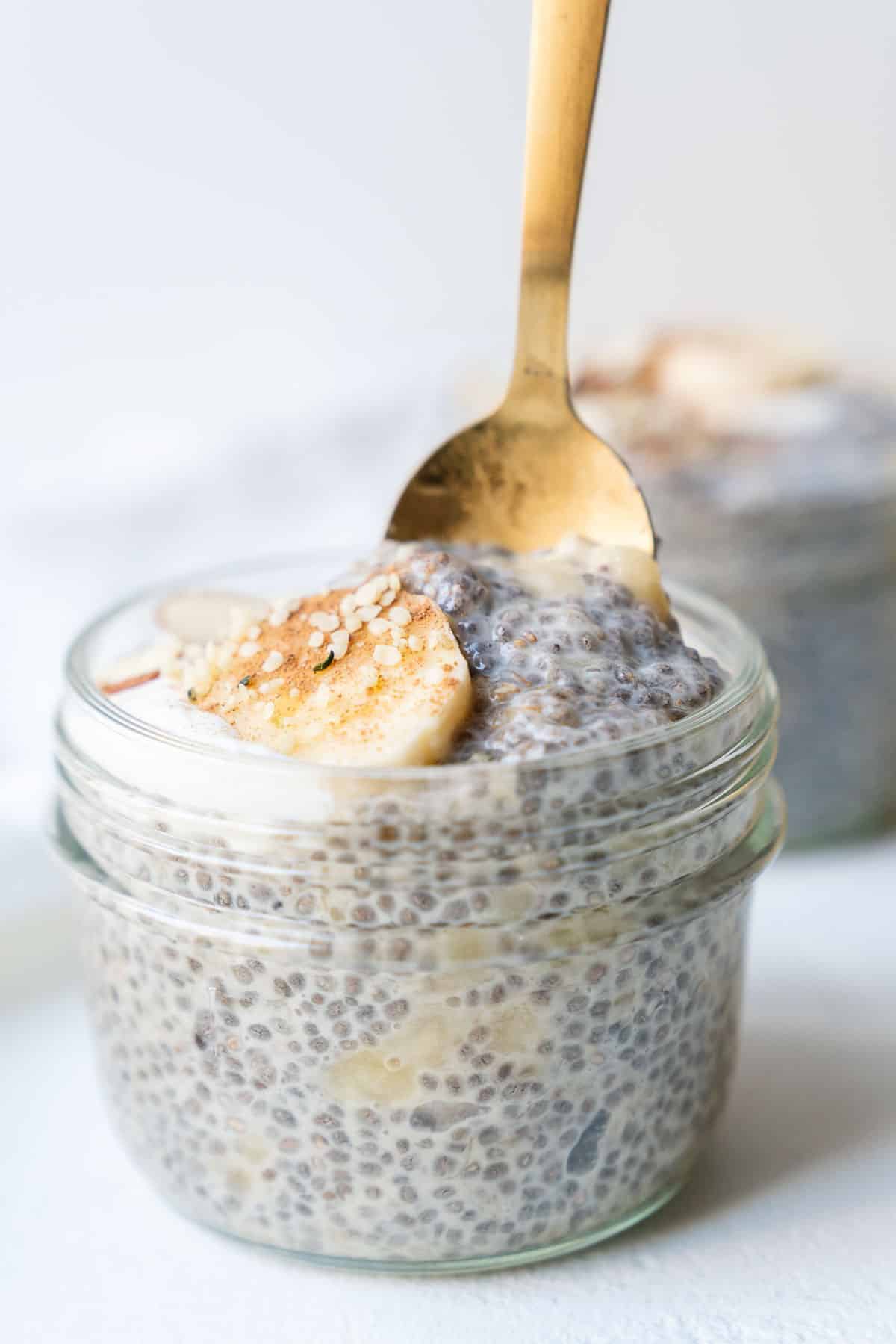 Glass jars of banana chia pudding with a gold spoon being dipped in.