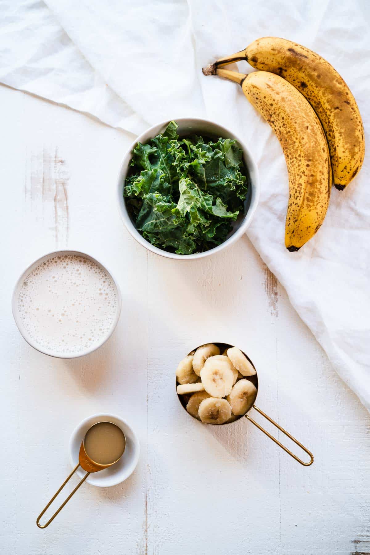 Ingredients for a banana kale smoothie on a white table.