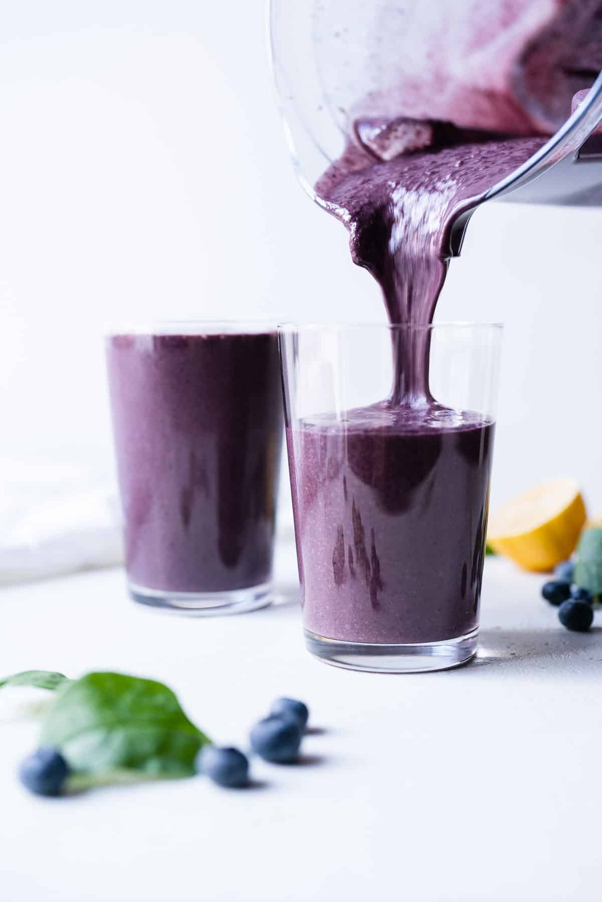 A blueberry spinach smoothie being poured into two clear glasses.