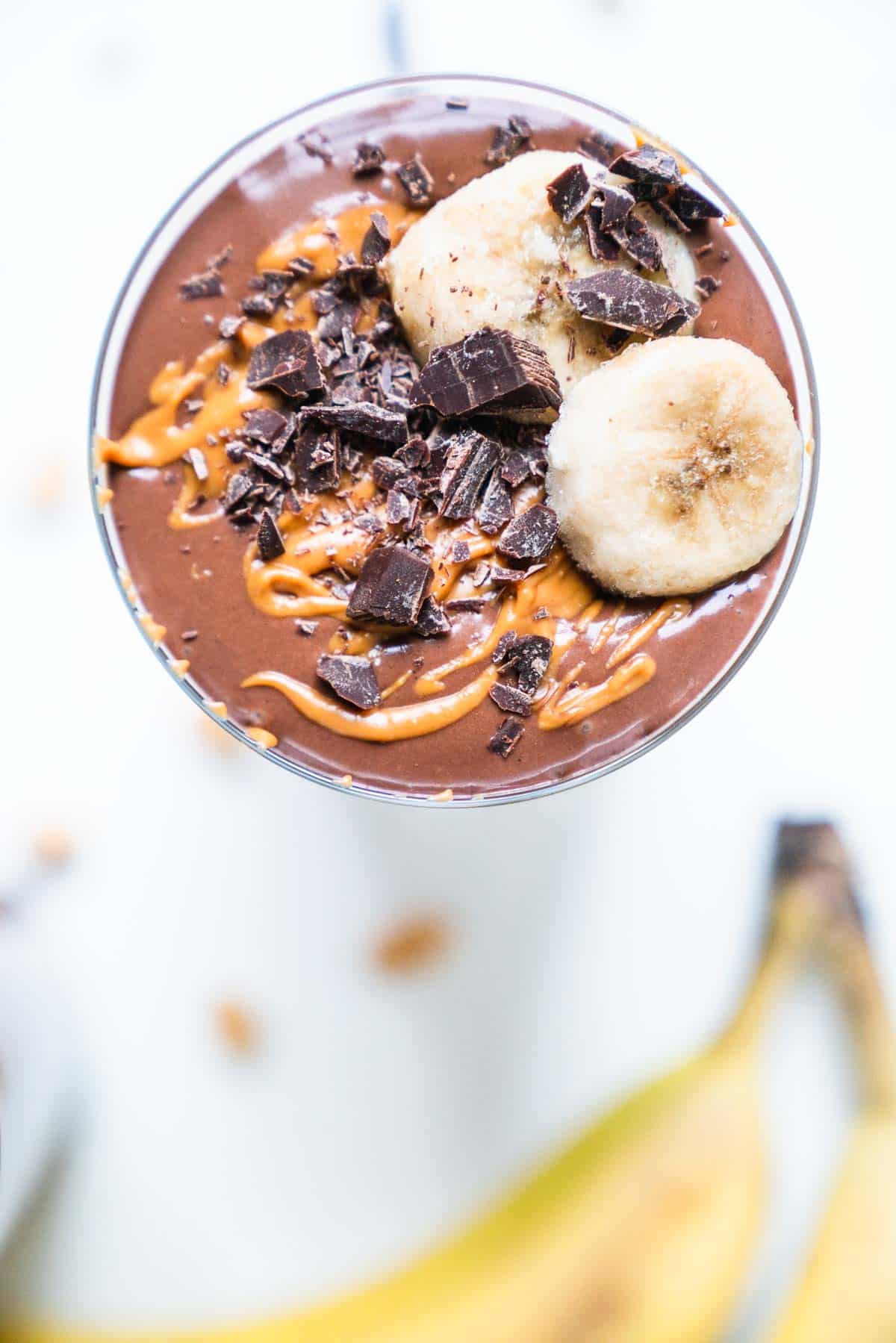 Overhead shot of a chocolate protein smoothie topped with peanut butter and banana slices.