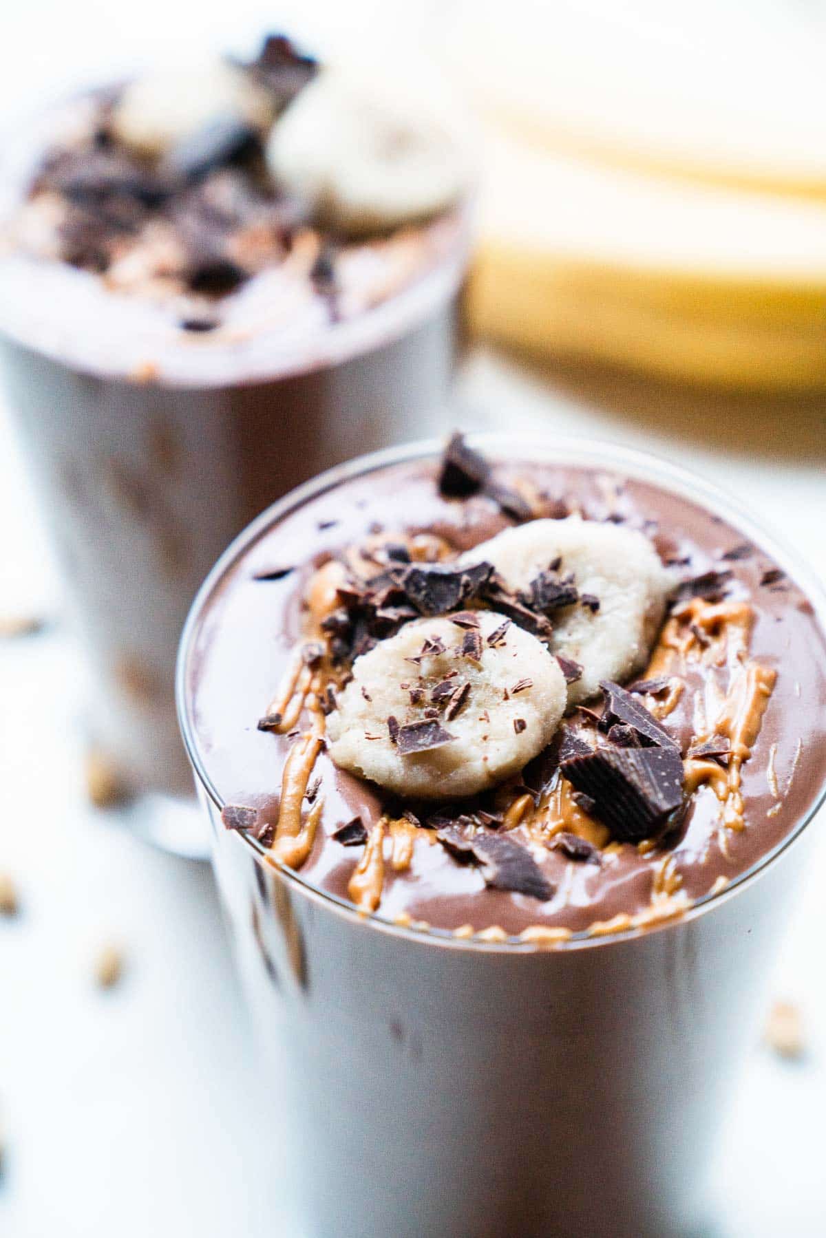 Two chocolate banana protein shakes topped with chocolate shavings and peanut butter.