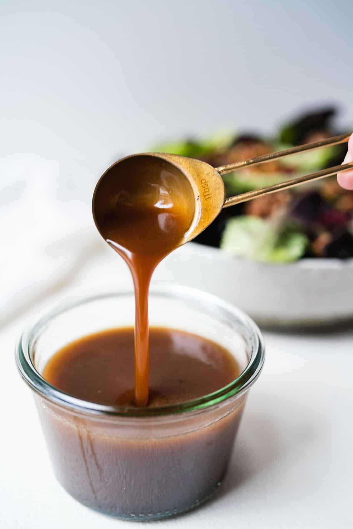 Honey balsamic vinaigrette being spooned out of a clear glass cup.