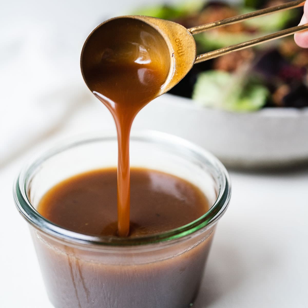 Honey balsamic vinaigrette being spooned out of a clear glass cup.