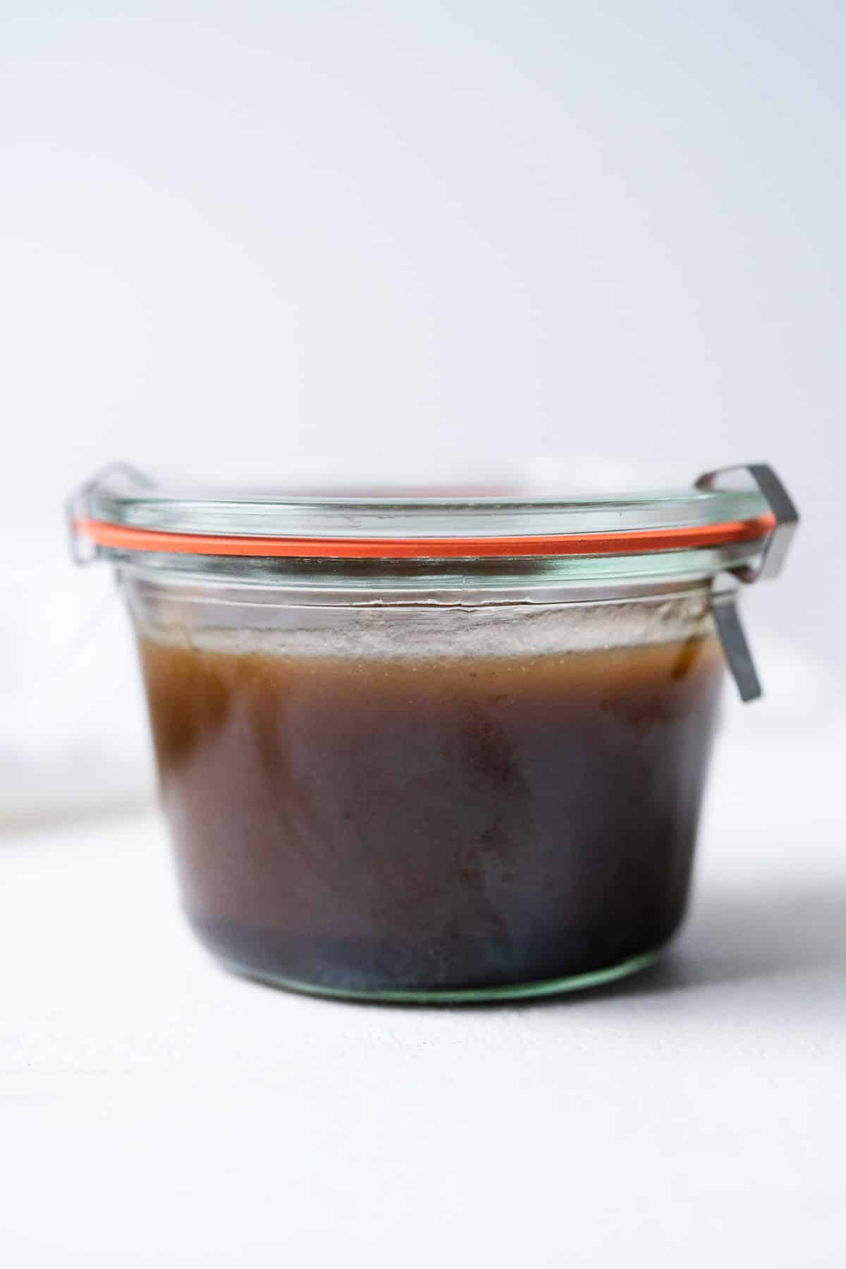 A glass jar filled with homemade dressing on a white table.