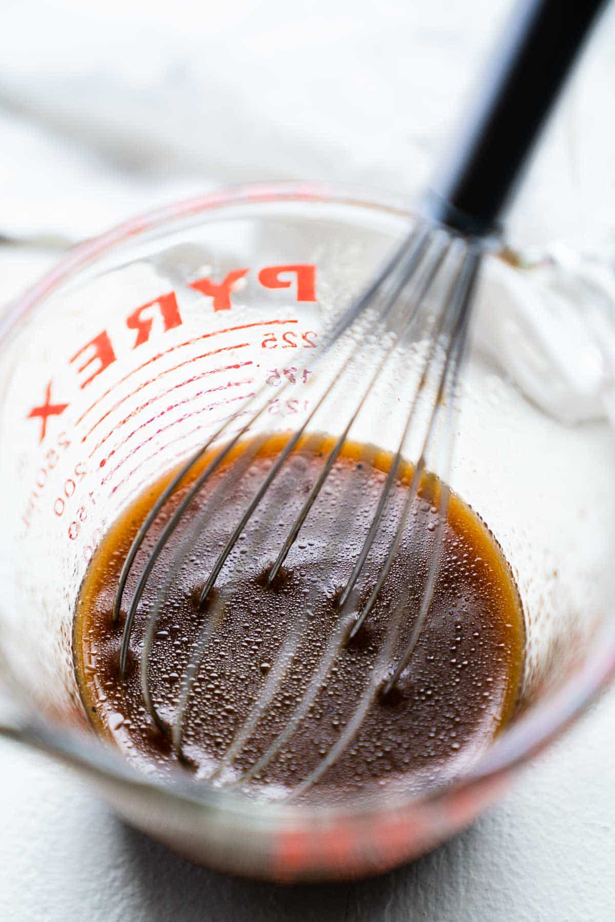 Whisking together a homemade dressing in a clear glass measuring cup.
