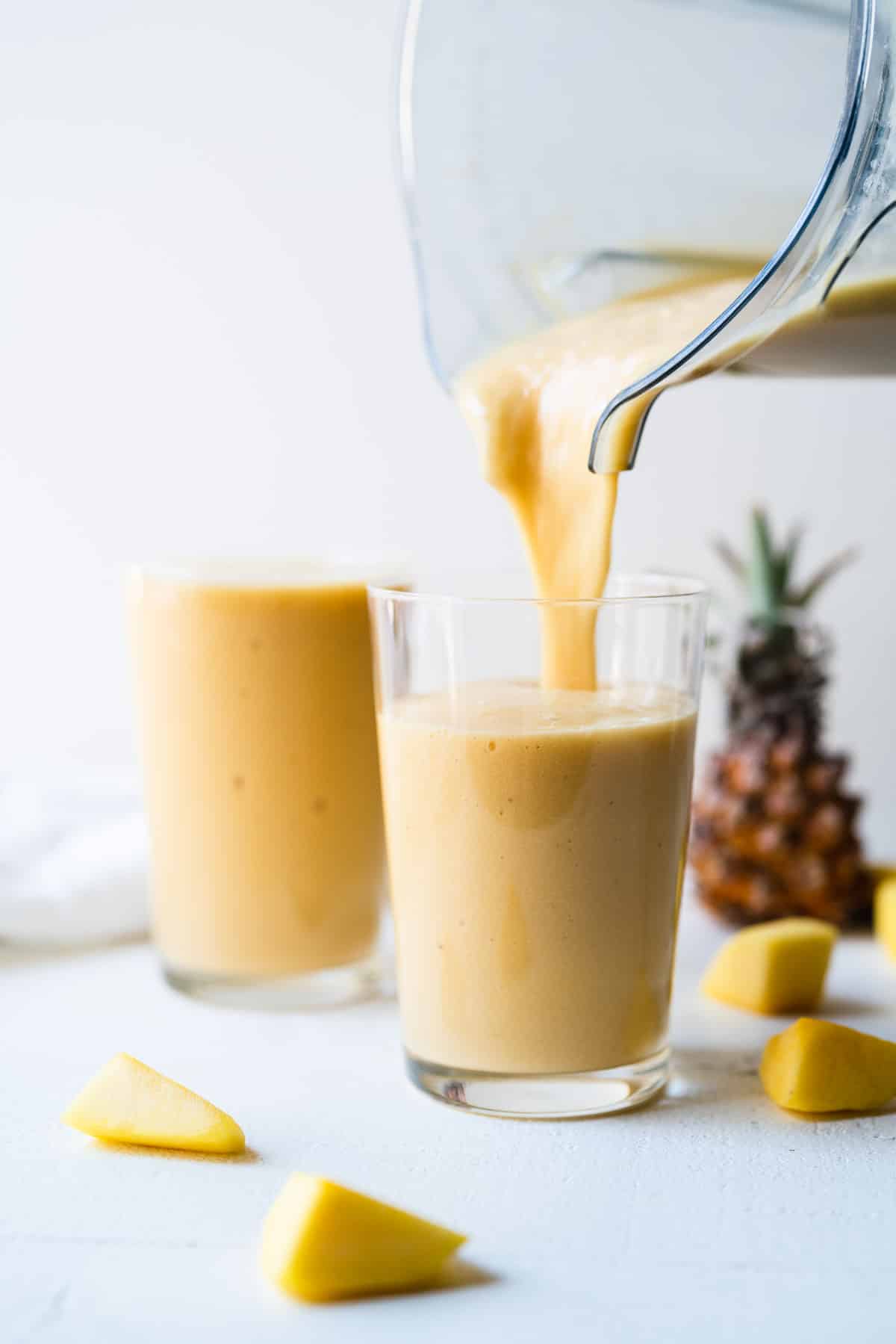 A mango pineapple smoothie being poured from a blender into a clear glass.