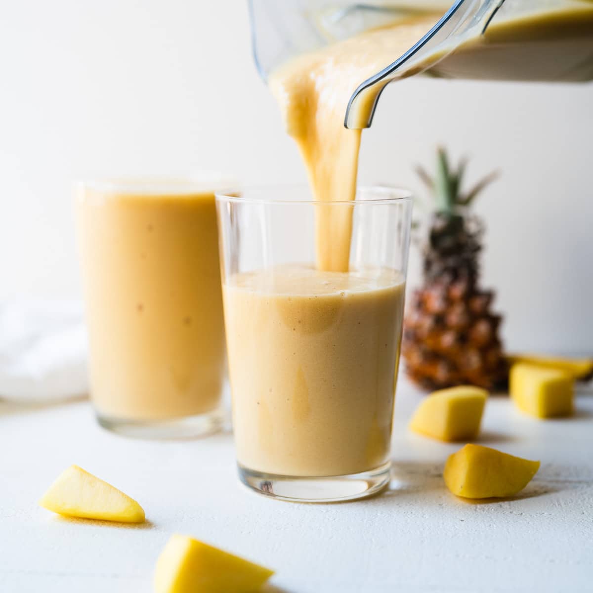 A mango pineapple smoothie being poured from a blender into a clear glass.