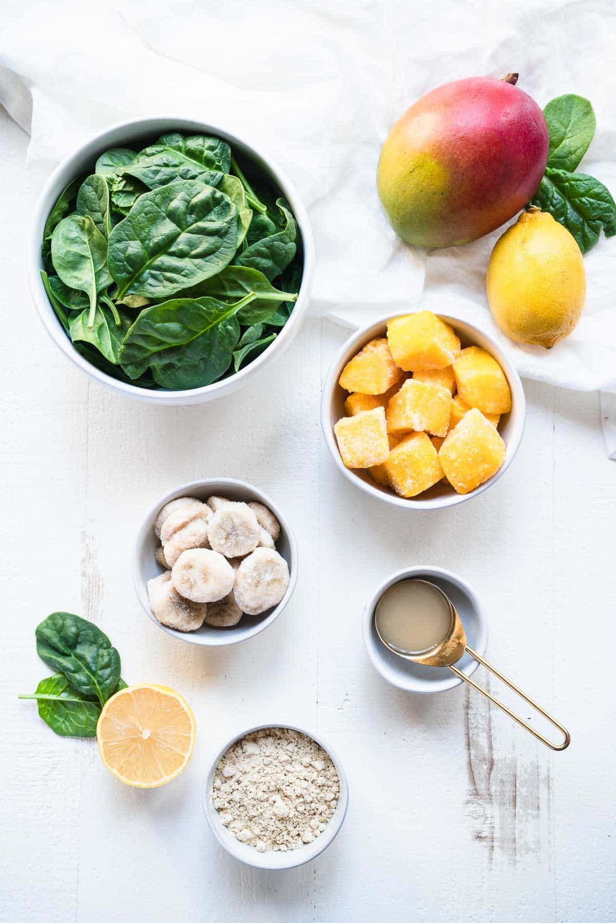 Ingredients for a mango spinach smoothie on a white table.