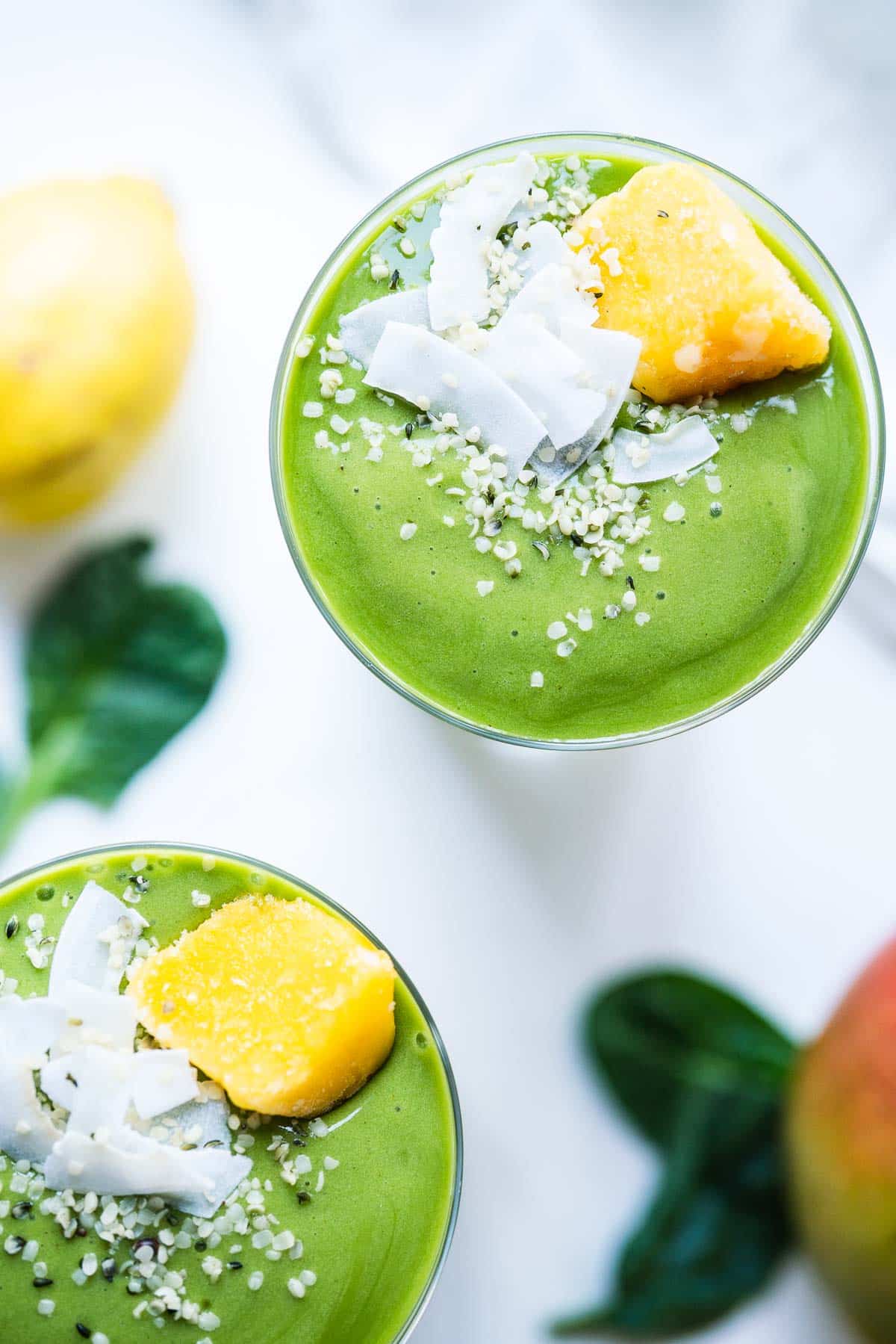 Two green smoothies topped with hemp seeds, coconut flakes and frozen fruit.