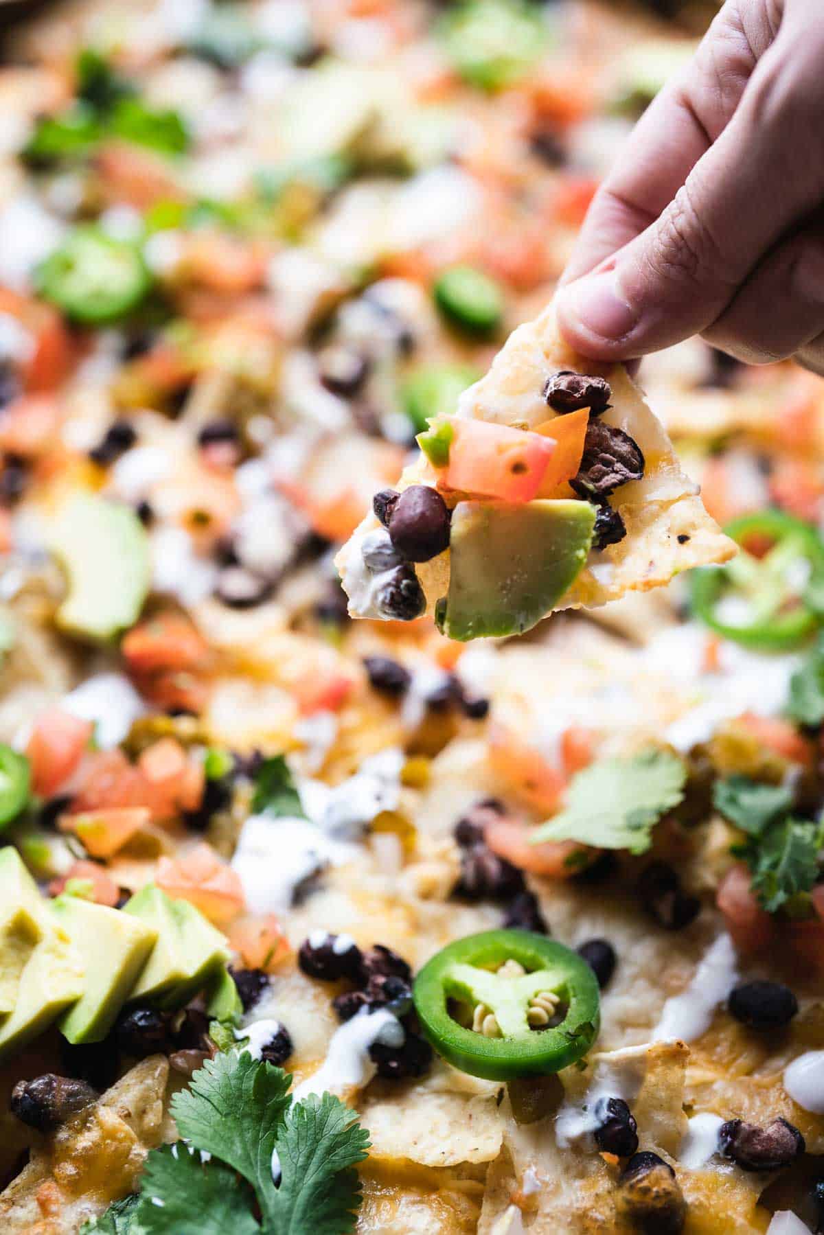 A single chip being pulled from a sheet tray of nachos.