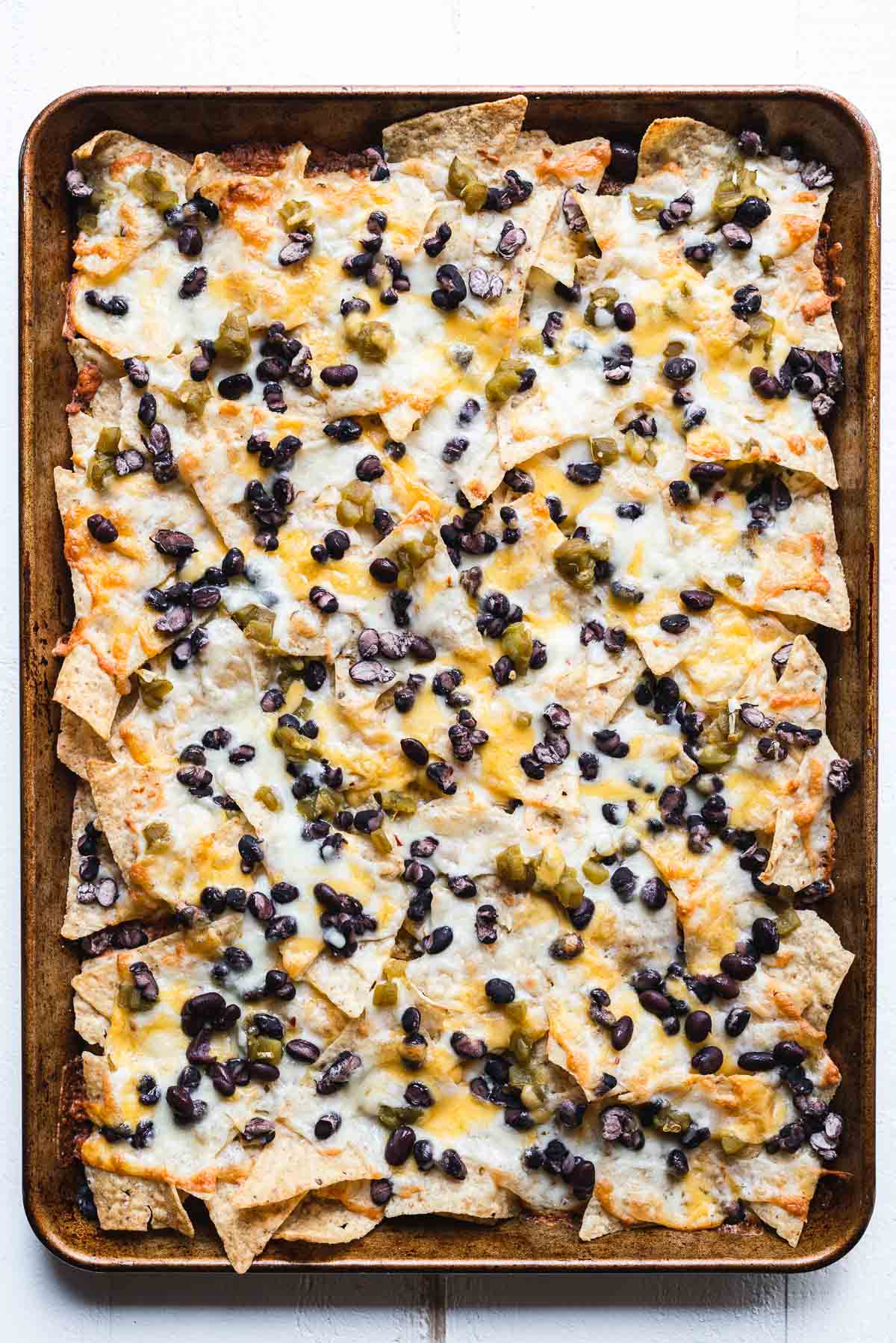 Oven baked nachos on a sheet tray on top of a white table.