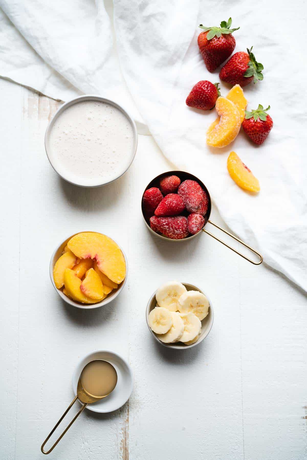 Ingredients for a strawberry peach smoothie on a white table.