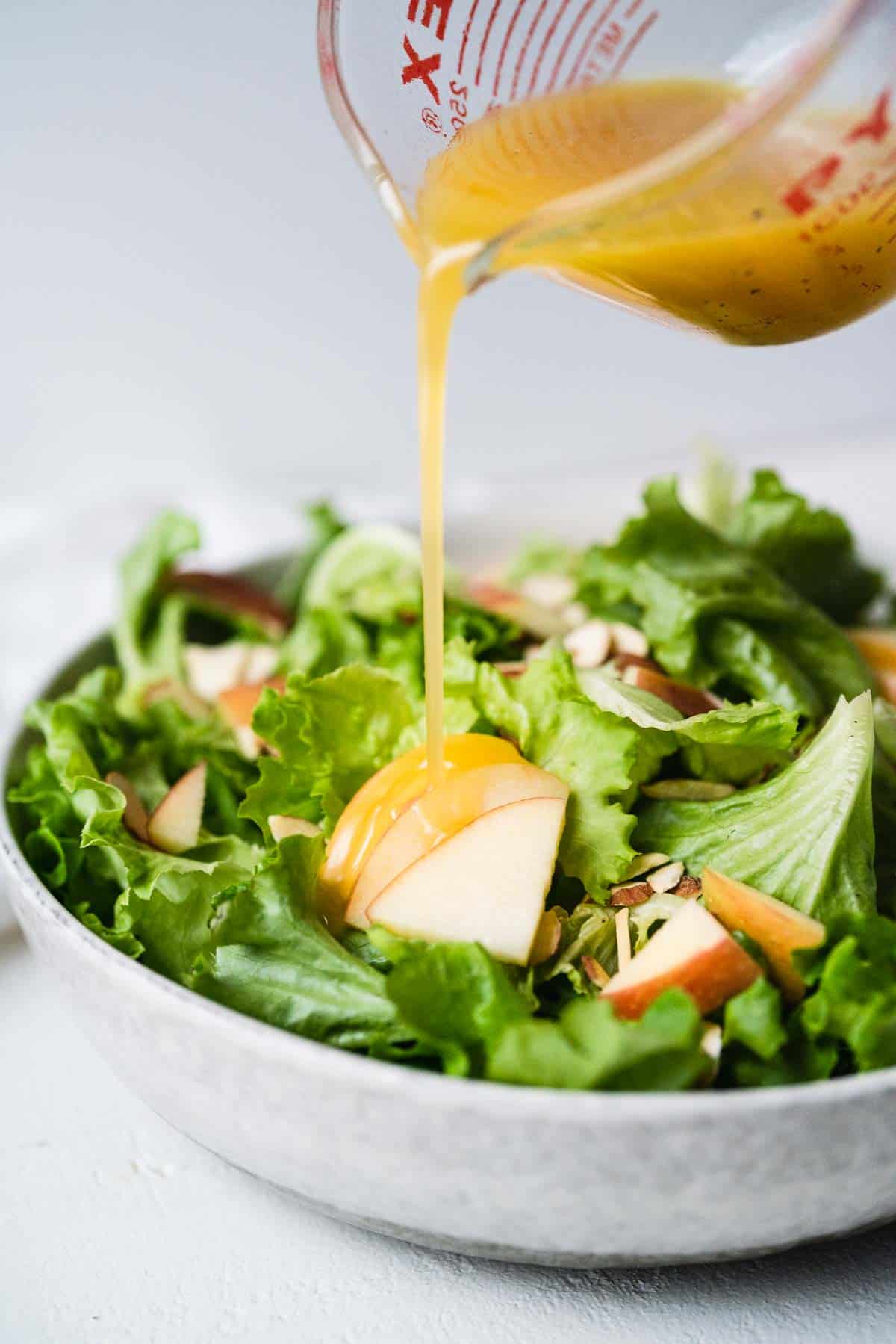 Salad dressing being drizzled over a green salad with fuji apples.