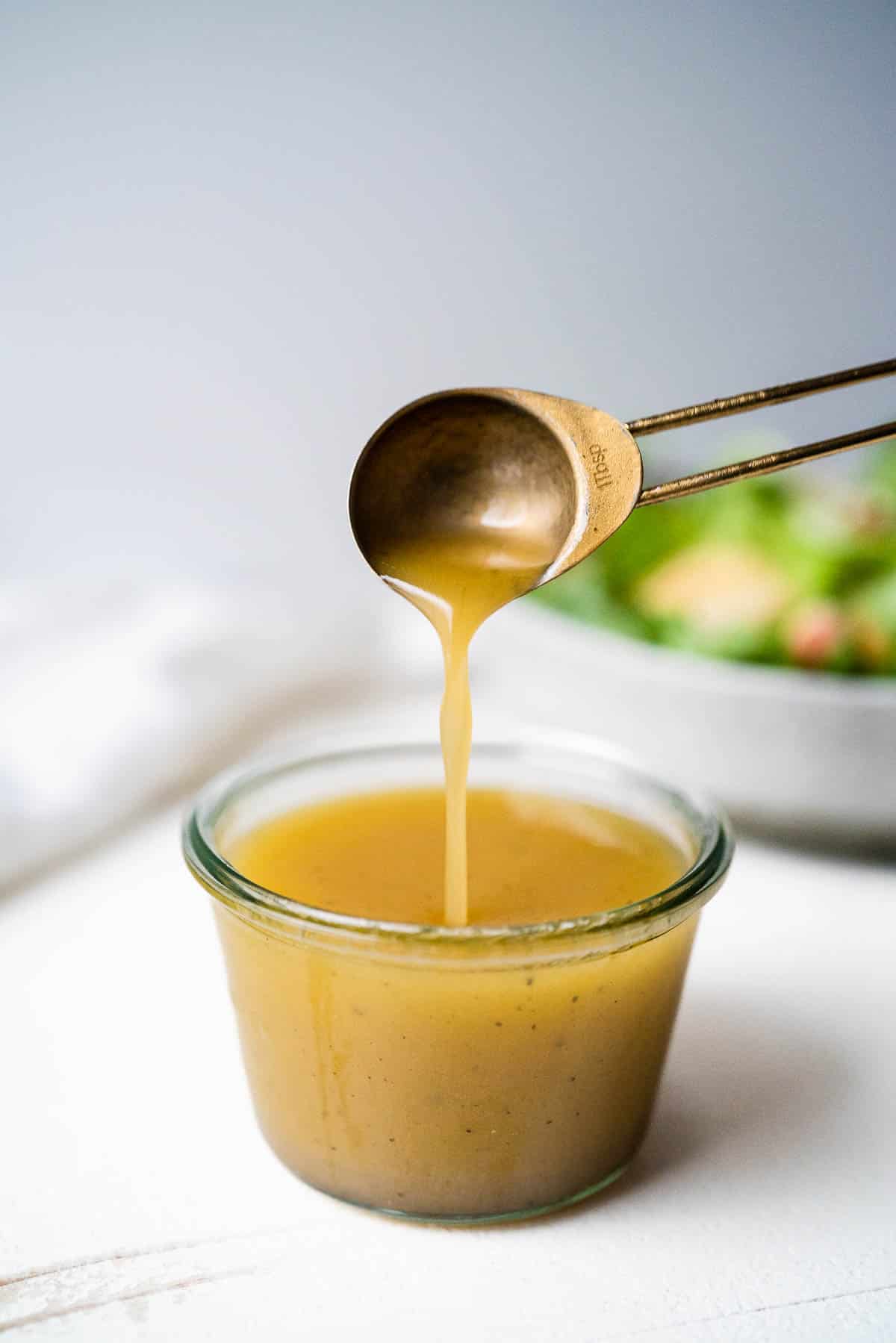 A spoon being lifted out of a jar of white balsamic dressing.