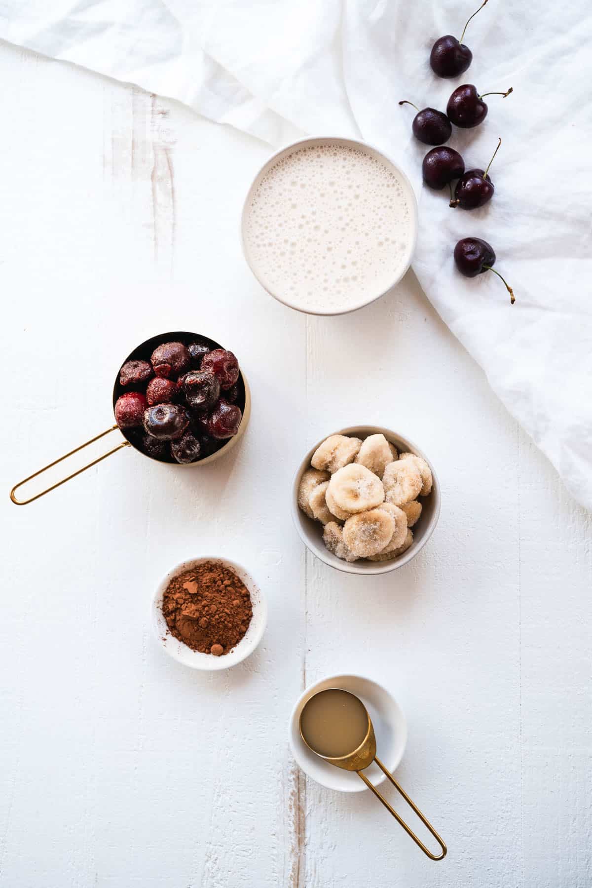 Ingredients for a chocolate cherry smoothie on a white table.