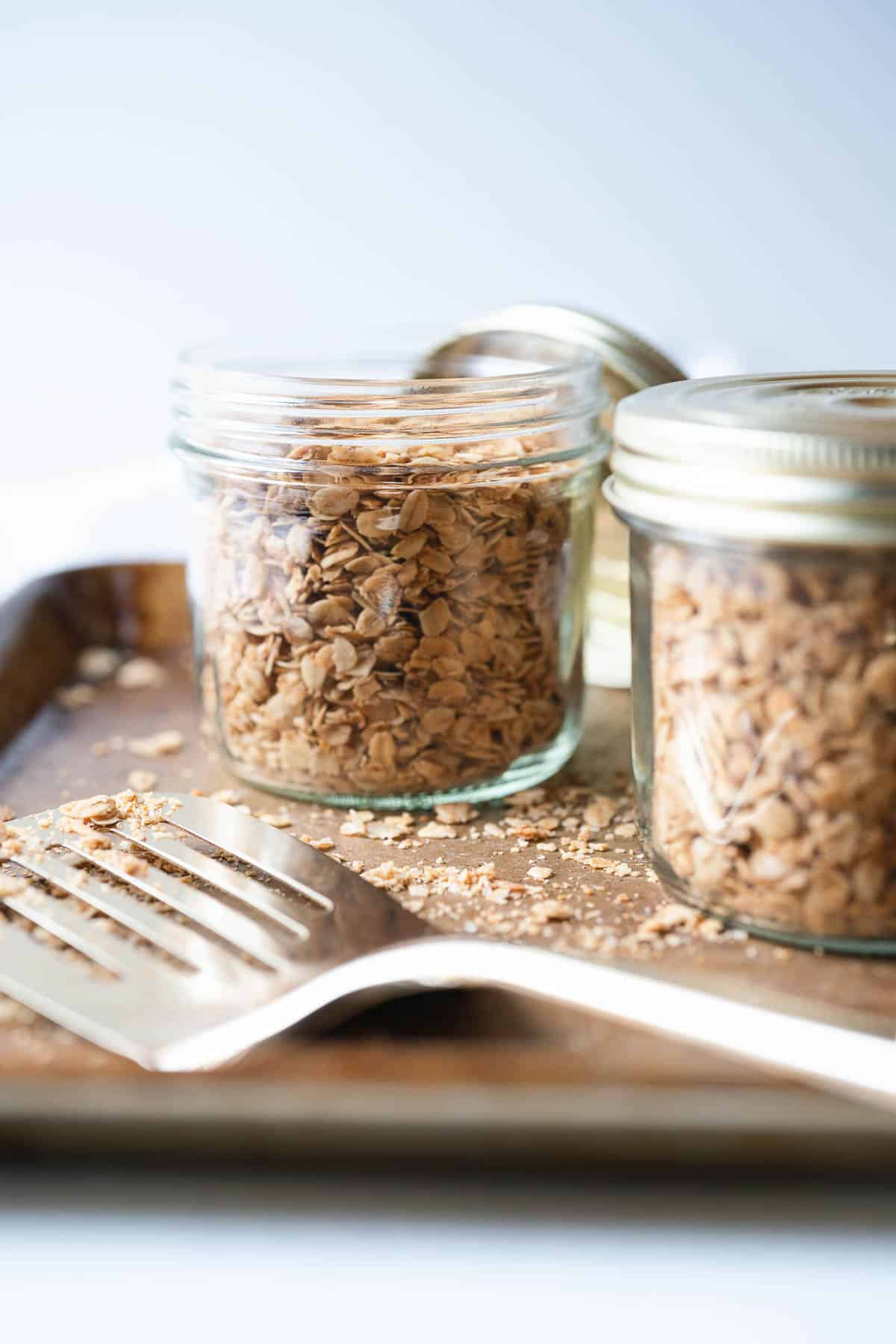 Two jar of nut free granola with a gold spatula in the front.