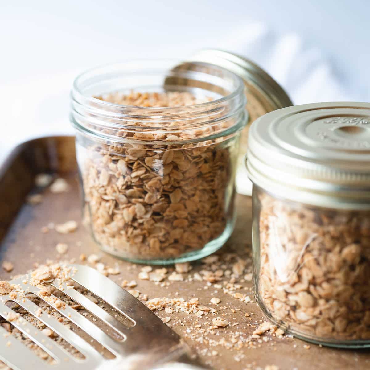 Two jars of nut free granola with a gold spatula in the front.