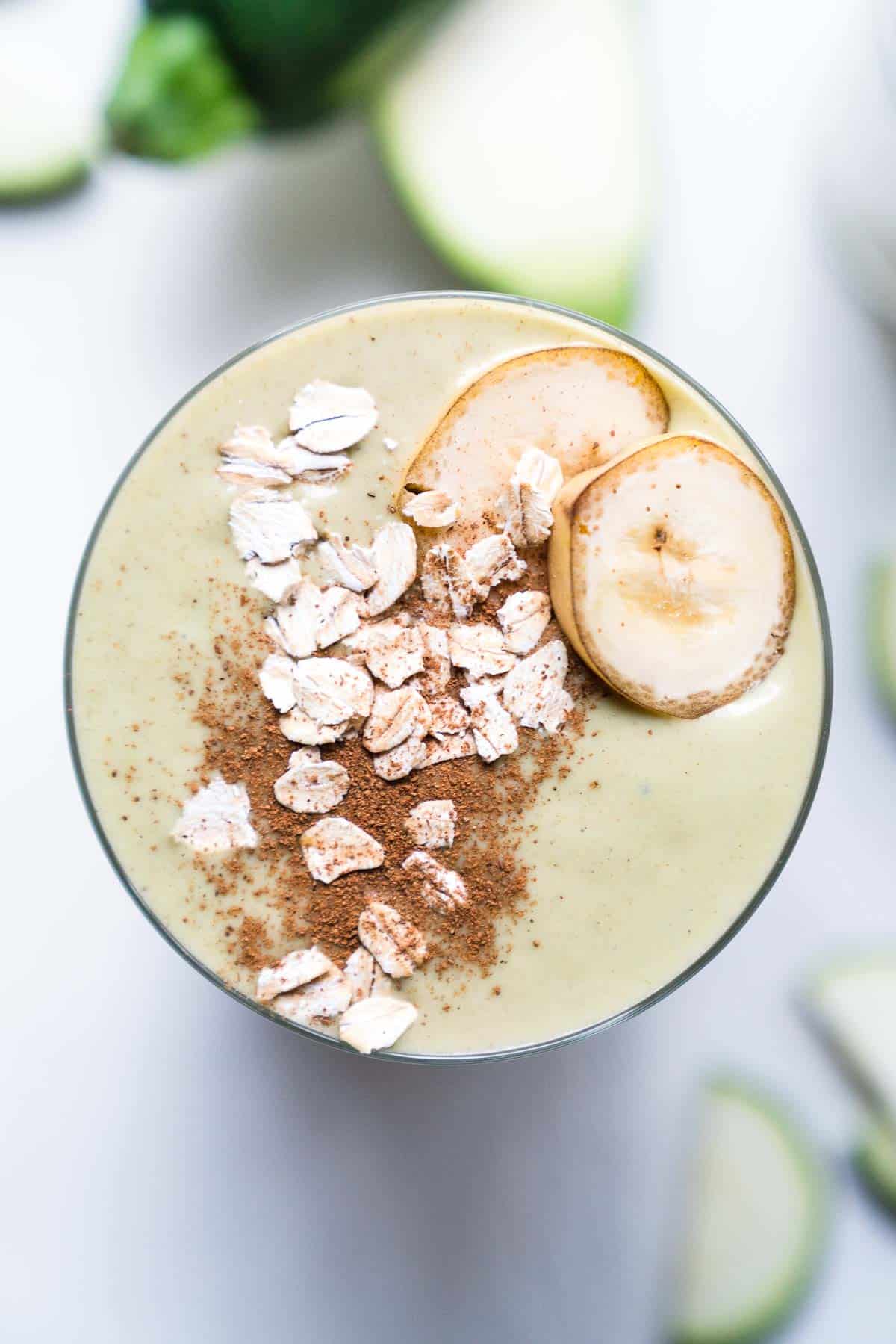 Close up of a zucchini smoothie topped with oats, with sliced vegetables in the background.