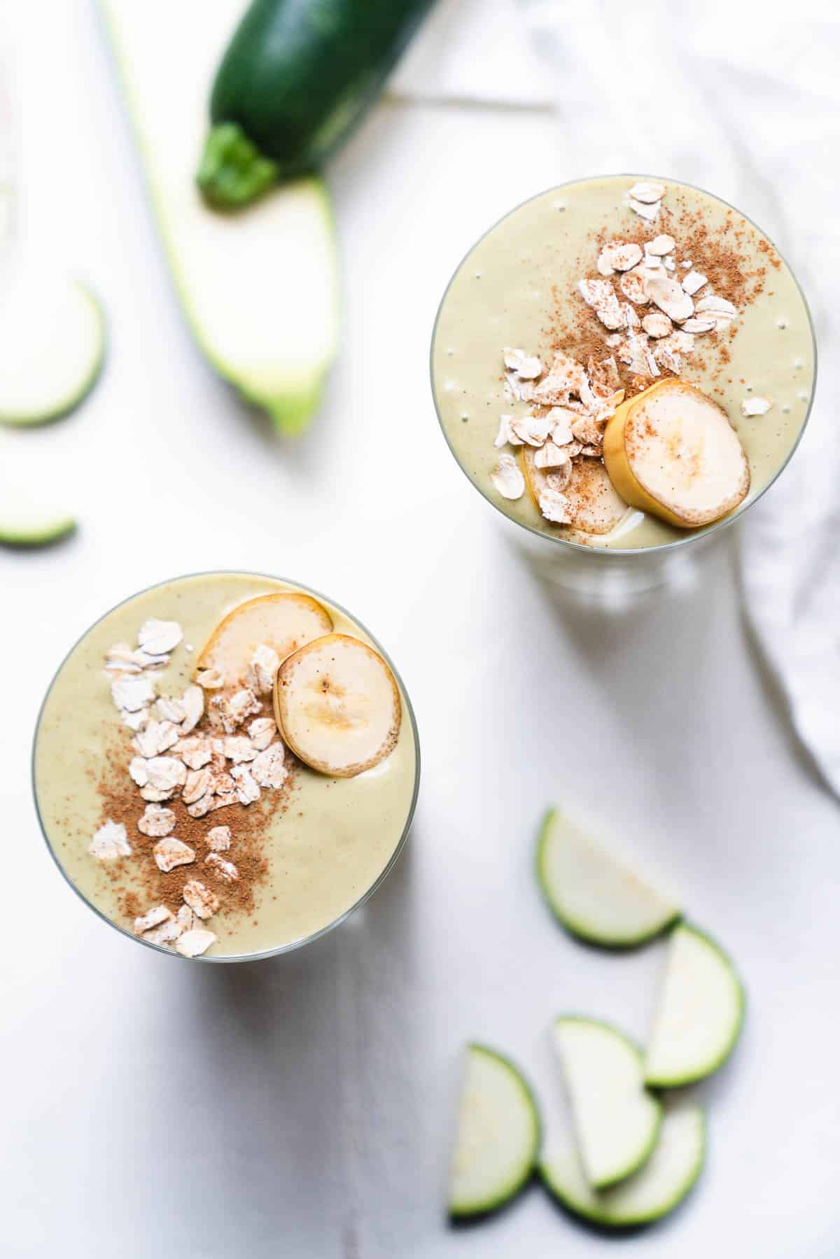 Two zucchini smoothies topped with rolled oats, cinnamon and sliced bananas.
