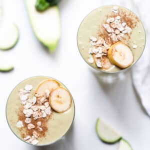 Two zucchini smoothies topped with rolled oats, cinnamon and sliced bananas.